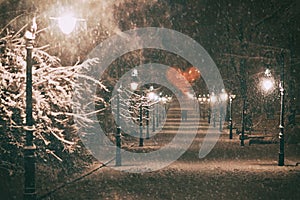 Couple in love on a romantic date walks through the snowy night winter park alley with beautiful lanterns covered with