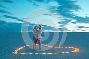 Couple in love romantic hugs in sand desert. Evening, romantic atmosphere, in sand burn candles in form of heart