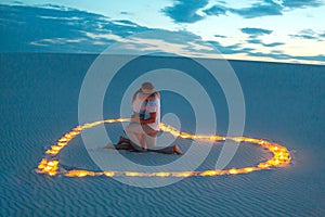 Couple in love romantic hugs in sand desert. Evening, romantic atmosphere, in sand burn candles in form of heart