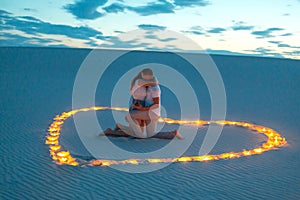 Couple in love romantic hugs in sand desert. Evening, romantic atmosphere, in sand burn candles in form of heart