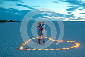 Couple in love romantic hugs in sand desert. Evening, romantic atmosphere, in sand burn candles in form of heart