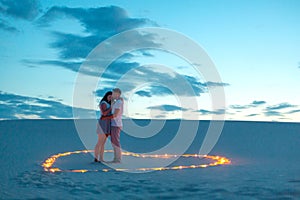 Couple in love romantic hugs in sand desert. Evening, romantic atmosphere, in sand burn candles in form of heart