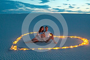 Couple in love romantic hugs in sand desert. Evening, romantic atmosphere, in sand burn candles in form of heart