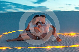 Couple in love romantic hugs in sand desert. Evening, romantic atmosphere, in sand burn candles in form of heart