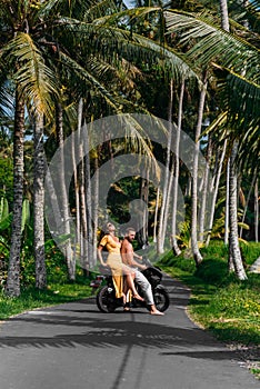 A couple in love on a scooter among the palm trees. Happy couple on vacation in Bali. The couple travels the world. Vacation in