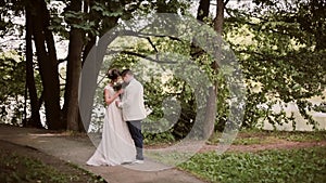 Couple in love share their wedding day. They happily stand in a park and smell beautiful brides bouquet.