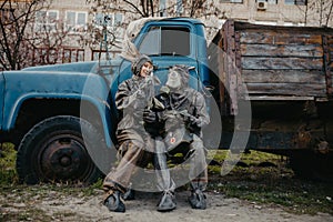 Couple in love sits in NBC protective suits and gas mask near old truck