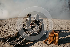 Couple in love sits at outing in NBC protective suits and gas masks on smoke background