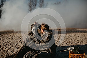 Couple in love sits at outing in NBC protective suits and removes gas masks on smoke background