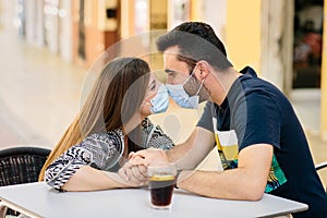 Couple in love sitting in a bar tries to kiss each other with a mask on their faces