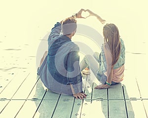 Couple in love sitting on the pier, their hands show heart