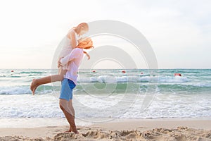 Couple in love. Smiling asian young man is holding girlfriend in his arms on the beach on evening time.