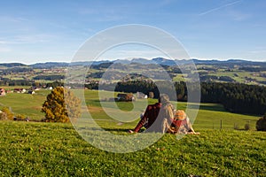 Couple in love stays on green grass looking at hills and mountains in autumn , sourrounded by beautiful rural landscape from