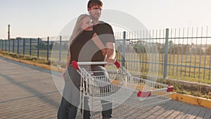 Couple in love in a supermarket parking lot with a trolley from the store at sunset. Slow motion