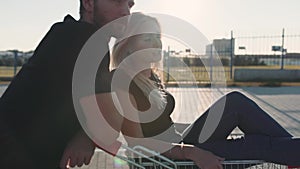 Couple in love in a supermarket parking lot with a trolley from the store at sunset. Slow motion