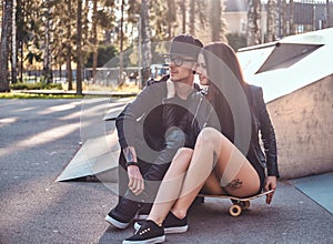 Couple in love together sits on a skateboard in a skate park at the summertime