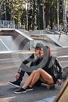 Couple in love together sits on a skateboard in a skate park at the summertime