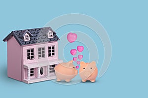 Couple in love, two piggy bank with wooden house on a bright blue background