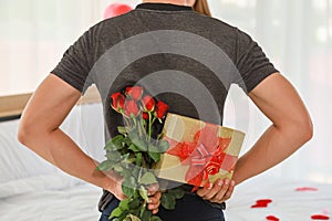 Couple, Love and Valentine`s Day Concept. Back of man surprised his girlfriend with a gift box and rose in bedroom