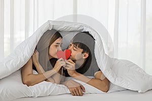 Couple, Love and Valentine`s Day Concept. Portrait of two asian man and woman on bed in white blanket and holding red paper heart