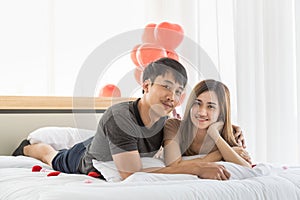 Couple, Love and Valentine`s Day Concept. Portrait of two smiling asian man and woman laying on bed in bedroom and looking to