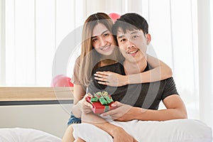 Couple Love and Valentine`s Day Concept. Young smiling Asian man and woman looking to camera with beautiful giving gift box on be