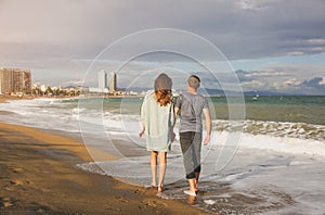 Couple in love walking on the beach on sunny day. Stylish hipsters near the waves on the sea. Man and woman hugging and kissing.