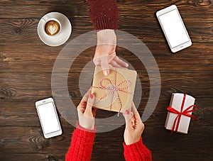 Couple in love. Woman give man present. Man and female hands top view on wooden table with phones and coffee cup