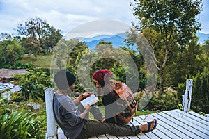 Couple lover natural travel on the mountain, sitting relax reading books in the midst of nature on the white wooden bridge