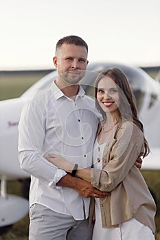 A couple of lovers, in the cockpit on their own plane. Smiling people and a private plane in the background.