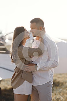 A couple of lovers, in the cockpit on their own plane. Smiling people and a private plane in the background.