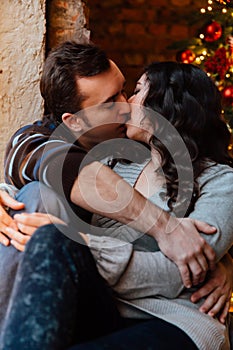 Couple of lovers hugs sitting on the windowsill in the Christmas loft studio. guy is hugging the girl.