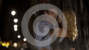 Couple of lovers looking at each other, hiding from rain under umbrella, date