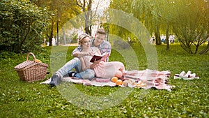 Couple of lovers reading novel book sitting on rug during picnic, romantic date