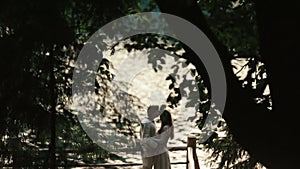 Couple of lovers softly embracing on the pier with chimerical patterns of branches on foreground. Magic love story in