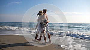 Couple of lovers walking at coast and holding hands during resting on resort. Man hugs woman strolling on beach and