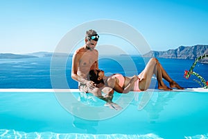 Couple on a luxury vacation in Greece, Oia Santorini men and woman at caldera infinity pool looking out over the ocean