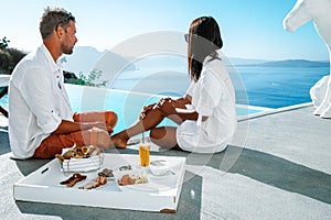 Couple on a luxury vacation in Greece, Oia Santorini men and woman at caldera infinity pool looking out over the ocean