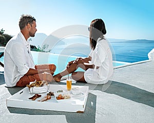 couple on a luxury vacation in Greece, Oia Santorini men and woman having breakfast at the pool