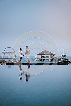 Couple on a luxury vacation in thailand walking by the ocean with pool and bleu sky