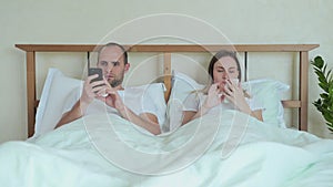 Couple lying in bed using mobile phone while ignoring each other. Man and woman addicted to smartphone social networks