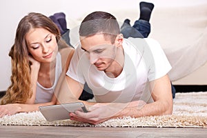 Couple lying on carpet and looking at tablet
