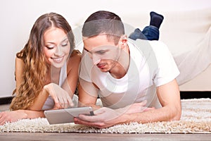 Couple lying on carpet and looking at tablet