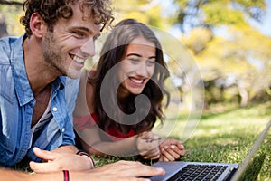 Couple lying on grass and using laptop