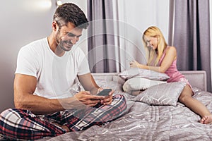 Couple lying separate in a bed, man using phone