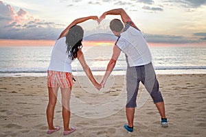 Couple making heart shape with arms at sunset