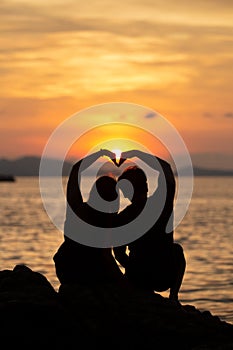 Couple making heart shape on the beach in sunset.