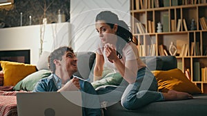 Couple making purchase online looking at laptop sitting couch cozy living room.