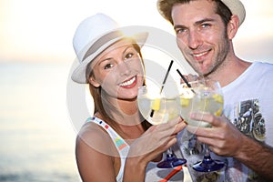 Couple making toast with cocktails on the beach