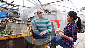 Couple of male and female hispanic workers talking and discussing something near forklift loader at farm